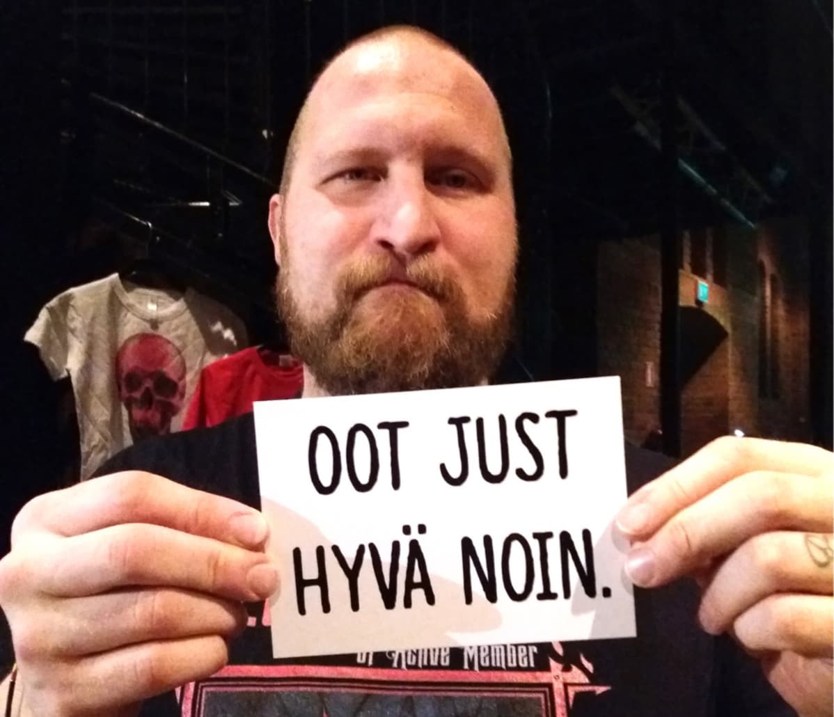 Rap-artisti Paleface esittelee Oot just hyvä noin -kampanjan pientä julistetta.