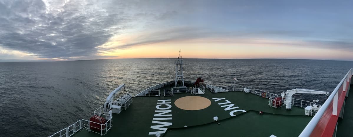 Laivan keula, edessä avovettä, horisontissa auringnlasku.
