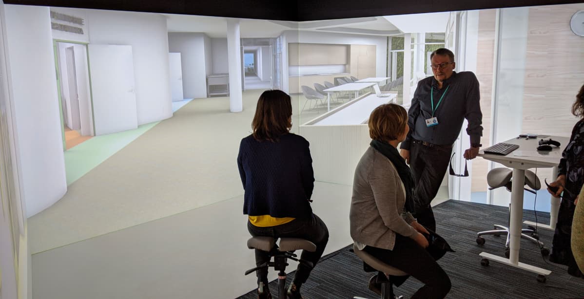 Joukko ylilääkäreitä ja ylihoitaja ovat tutustumassa suunnitteilla olevaan, uuteen Laakson yhteissairaalaan, 3D-huoneeseen projisoidun 3D-mallin avulla.