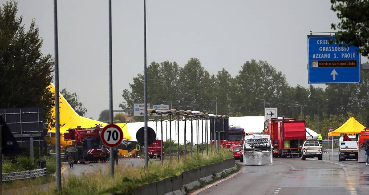 Kadun poikki liukunut lentokone kauempaa kuvattuna; sen edessä näkyy hälytysajoneuvoja ja liikennemerkkejä.