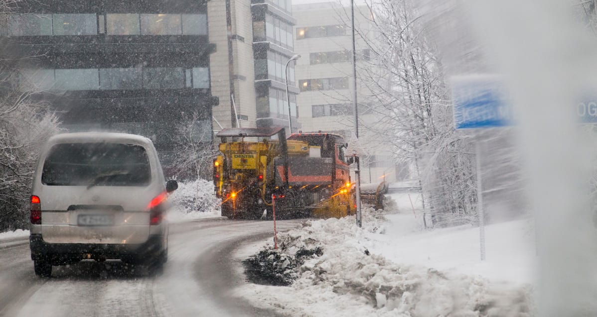 Pakettiauto ajaa lumiauran perässä sankassa lumisateessa