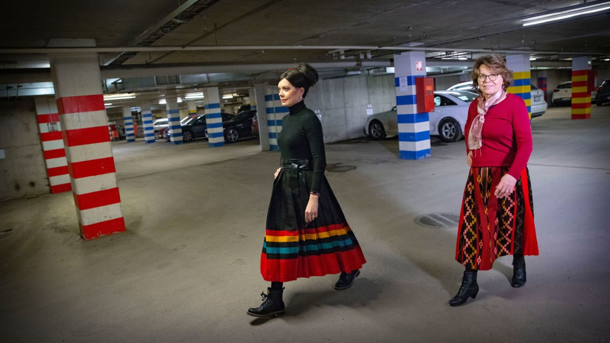 Naiset kävelevät parkkihallissa kansallispukujen hameet päällä