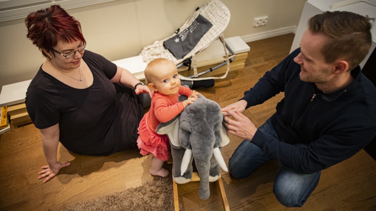 Taapero leikkii kiikkusnorsulla, ja vanhemmat seuraavat vierestä.