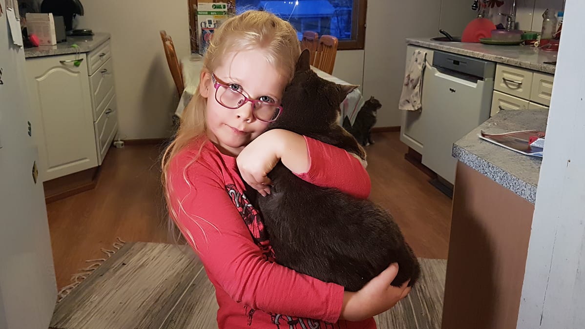 Helmi Penttilä seisoo keittiön ovella kissa sylissä.