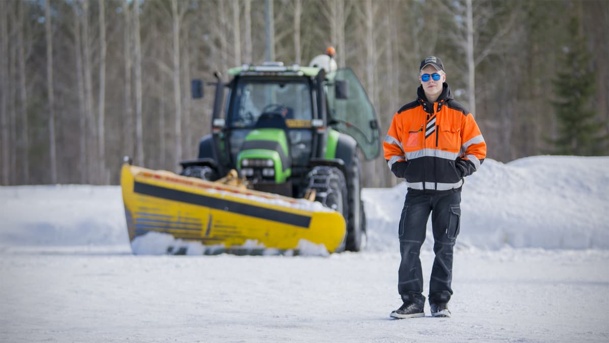 Nuori mies seisoo traktorin edessä.