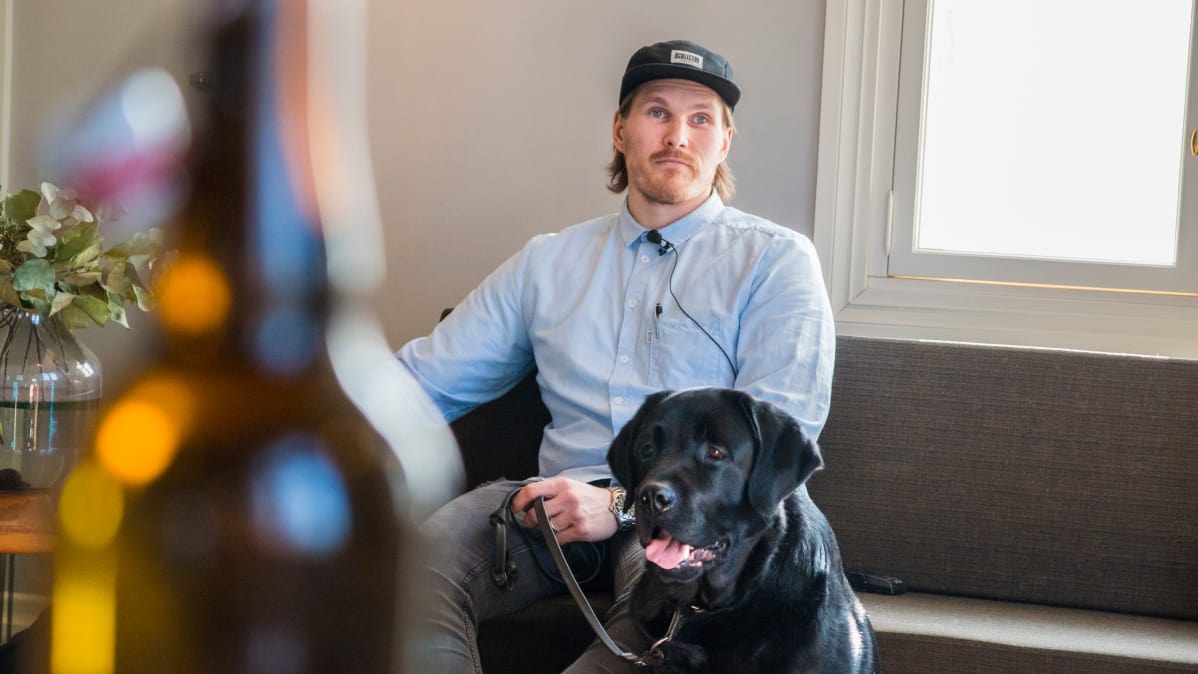 Mies istuu sohvalla vieressään musta labradorinnoutaja.