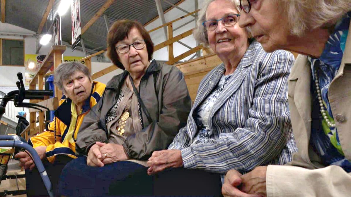 Neljä rouvaa istuu jäähallin penkillä.