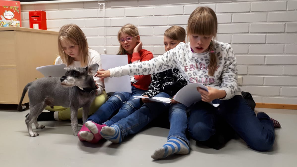 Koulukoira lukevien lasten keskellä