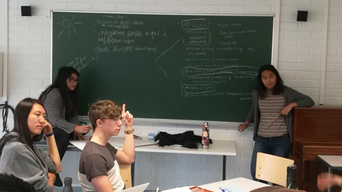 Liitutaululla vasemmalta: Alliana Marie Salanguit, Eva Wu, Jone Måsøy. Keskellä Kaustubh Srikanth. Oikealla takana Tasha Elizarde ja oikealla edessä Juhán Niila Stålka. Nuoret suunnittelevat luokassa julkilausumaansa.