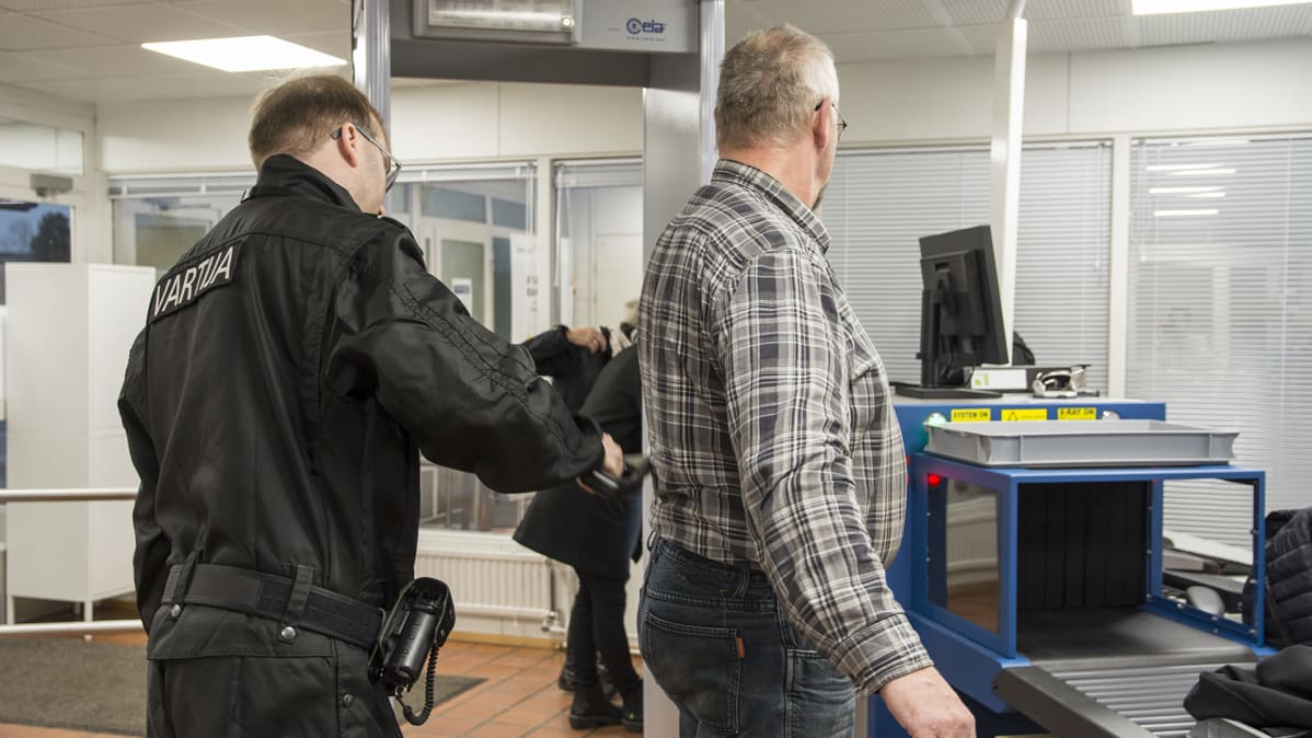 Vartija tarkastaa asiakasta oikeus- ja poliisitalon aulassa.