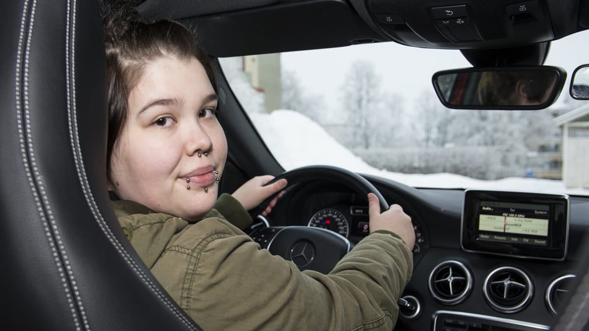 Nuori nainen istuu auton ratissa ja katsoo taakseen.