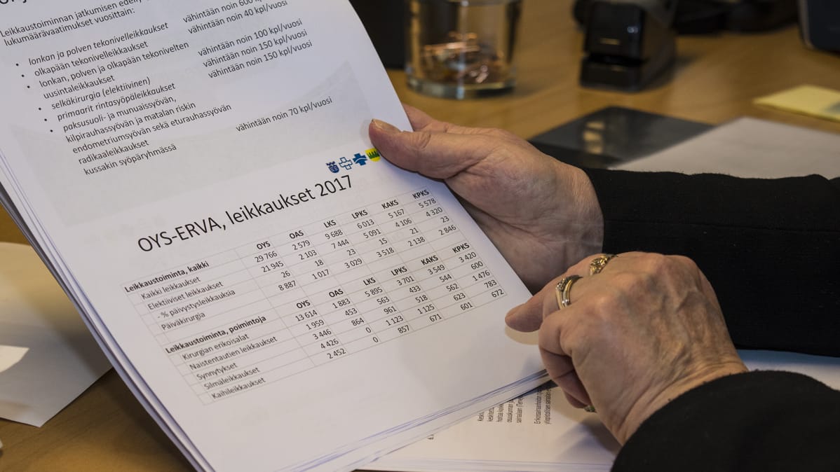 Nainen pitää käsissään paperia, mistä käy ilmi sairaalakohtaiset leikkausten lukumäärävaatimukset.