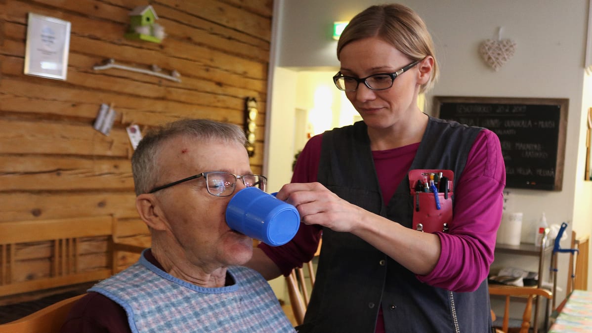 Tuija Juga auttaa asukasta juomaan