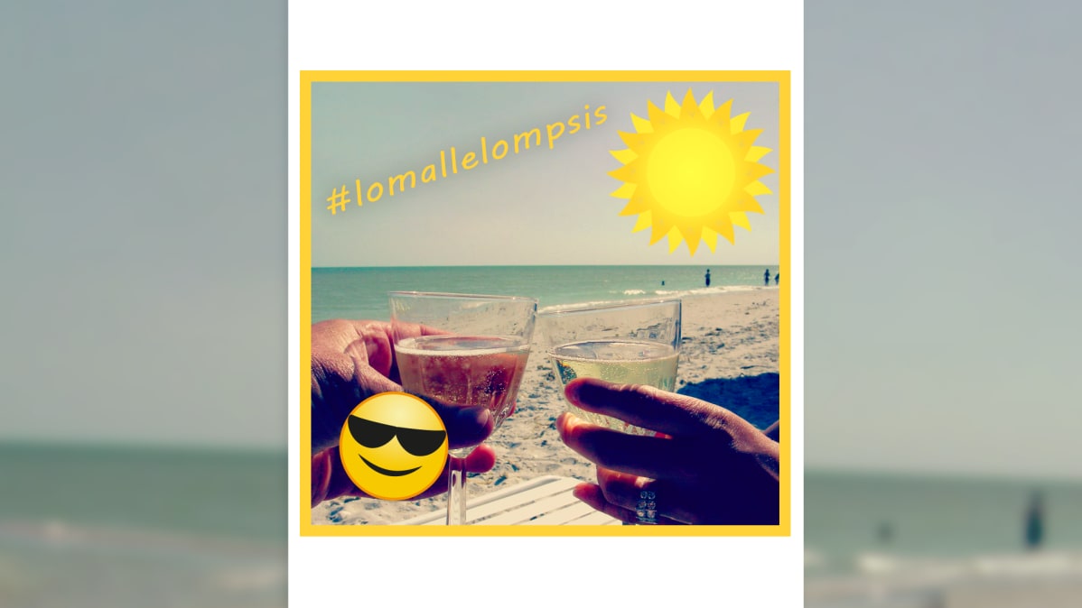 Kaksi viinilasia skoolaa uimarannalla. Teksti #lomallelompsis, auringon kuva, aurinkolasinen emojinaama