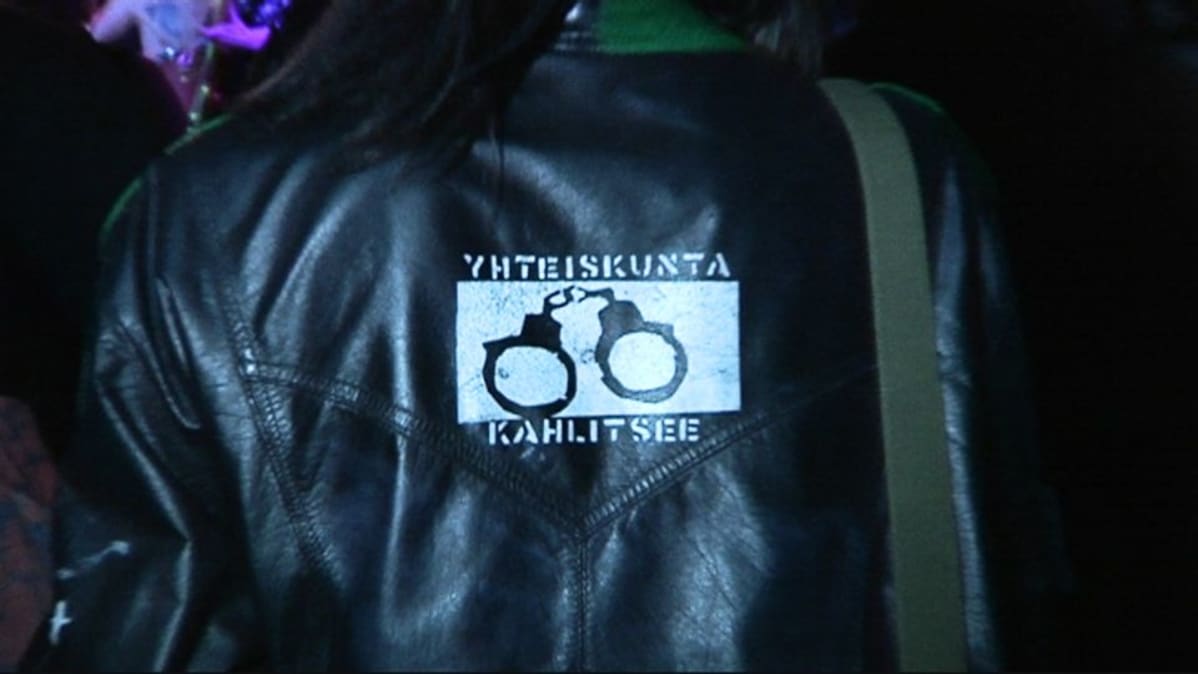 Nahkatakki, jossa lukee "yhteiskunta kahlitsee".