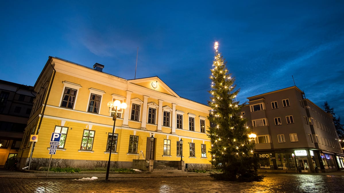 Joulukuusi Kokkolan Raatihuoneen edessä. Keltainnen rakennus, taustalla tummaa taivasta.