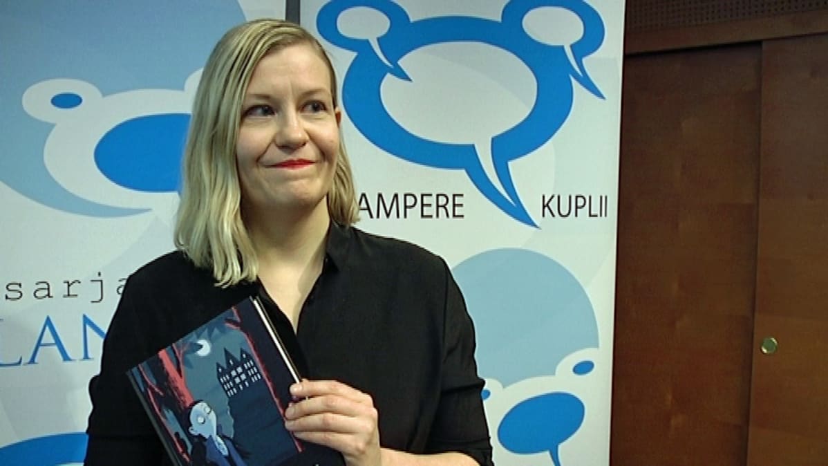 Kati Närhi seisoo palkitsemistilaisuudessa kirja kädessään.