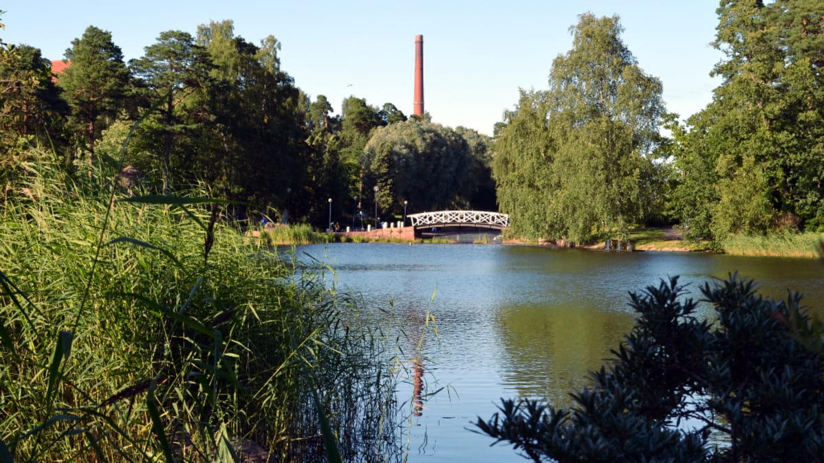 Koristeellinen kaarisilta ja teollisuuden savupiippu rinnakkain Kotkan Sapokan vesipuistossa.
