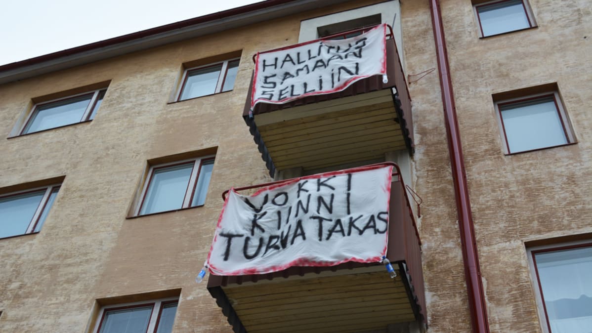 Parvekkeilta roikkuvia lakanoita, joissa iskulauseita.