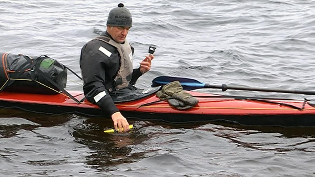Mies ottaa kanootissa järvivettä juomapulloon.