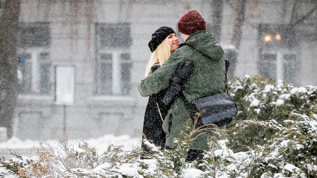 Nainen ja mies halaavat lumisateessa.