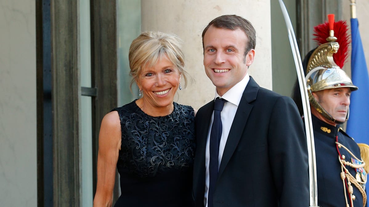 Brigitte Trogneux ja Emmanuel Macron vierekkäin palatsin ovella. Taustalla näkyy perinteisessä paraatiunivormussa oleva sotilas, joka pitää miekkaansa paljastettuna.