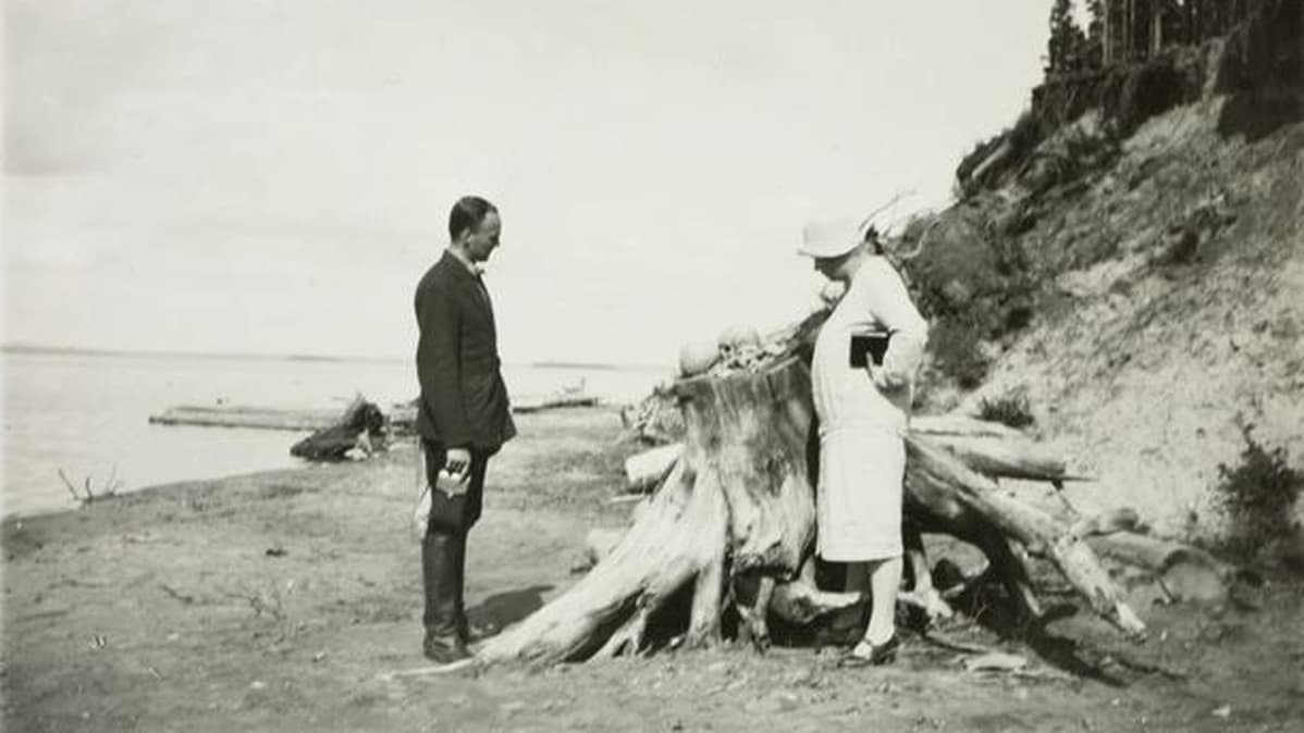 Mies ja nainen tarkastekevat järveen vyöryneen hatuausmaan paljastamia pääkalloja kannon päällä hiekkarannalla.