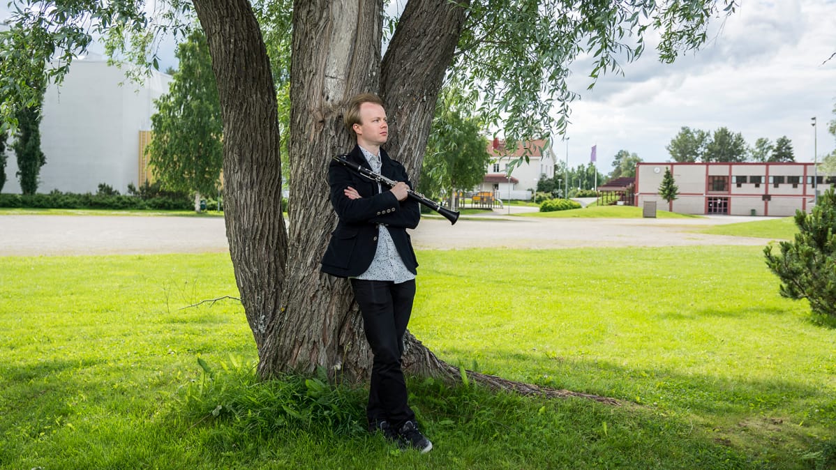 Lauri Sallinen nojaa puuhun Kuhmotalon vieressä.