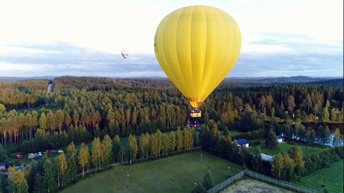 Keltainen kuumailmapallo lennossa.