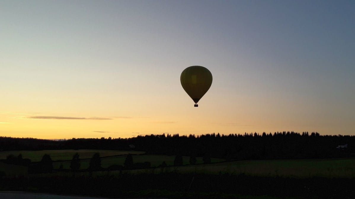 Kuumailmapallo lentää auringonlaskun maisemassa.