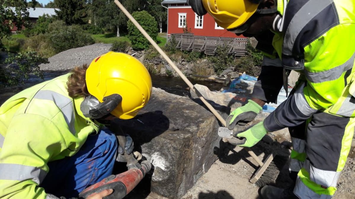 Miehet laittavat numerokilven kiinni kiveen.