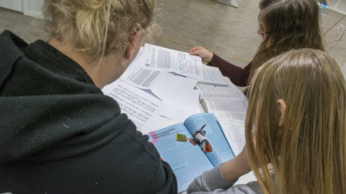 Opiskelijat selaavat opintomateriaalia pöydän ääressä.