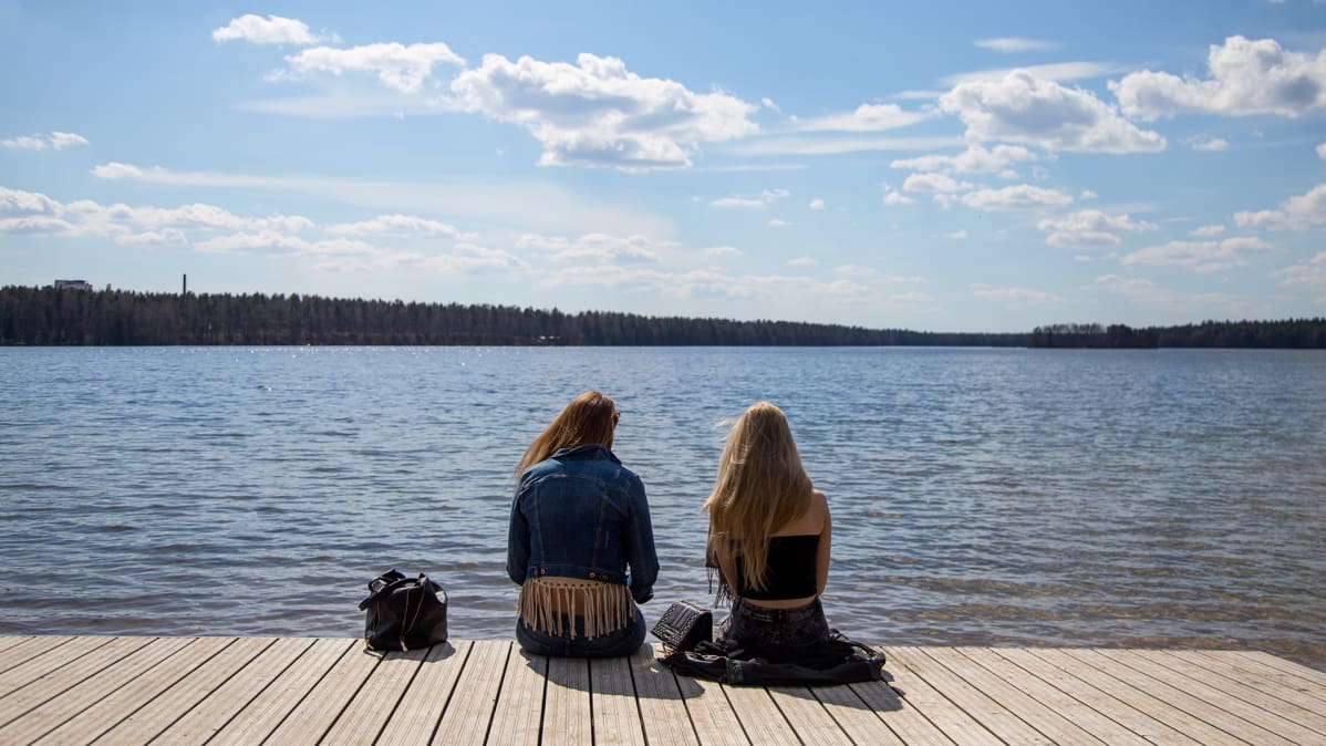 Kaksi nuorta naista istuu laiturilla järvellä keväällä.