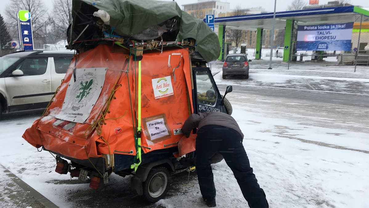 Mies tarkistaa parkkipaikalla täyteen lastattua tavaramopoansa