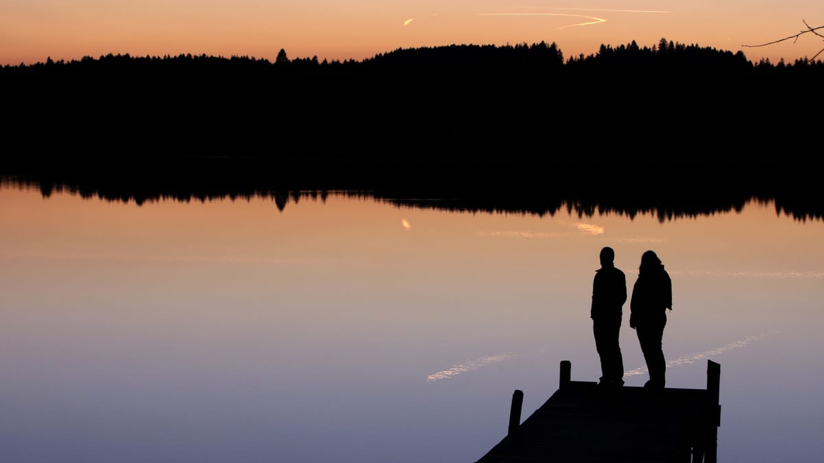 Pariskunta katselee auringonlaskua laiturilla.