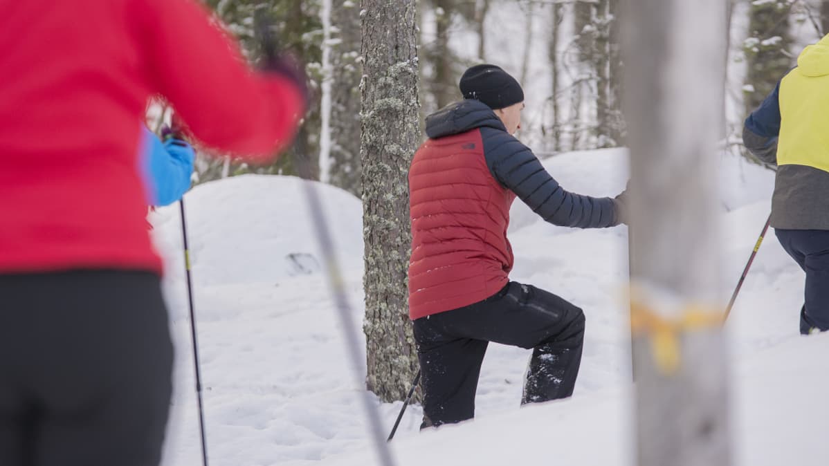 Lumikenkäilijöitä talvisessa metsässä.