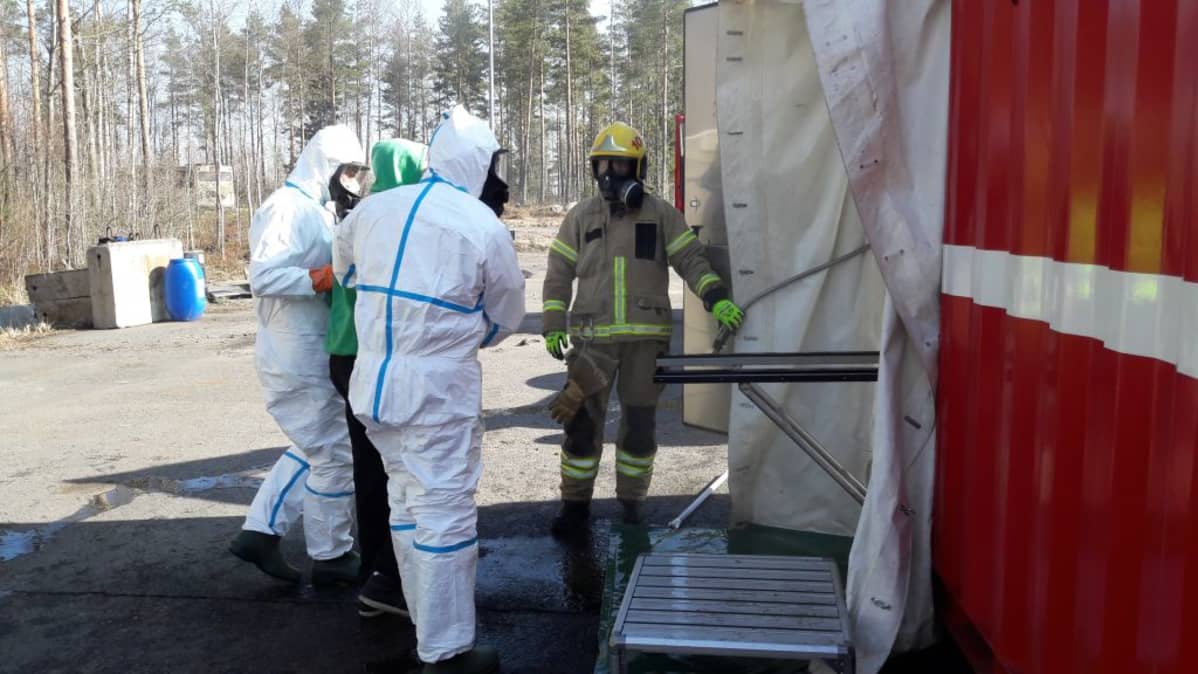 Suojapukuiset miehet vievät potilasta pesuun