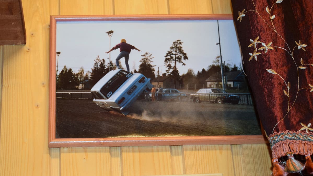 Kehyksissä kuva Kake Randelinista tasapainoilemassa auton katolla