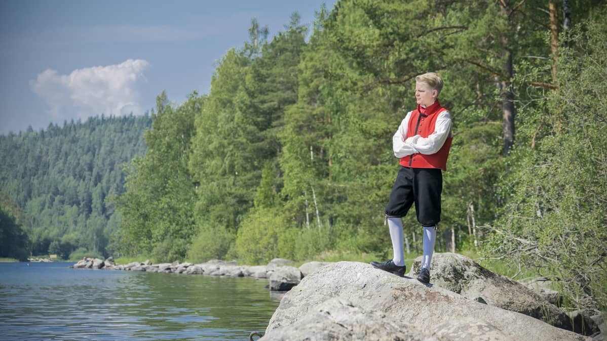 Jaakko Rikalainen kansallispuvussa koivu- ja järvimaisemassa.