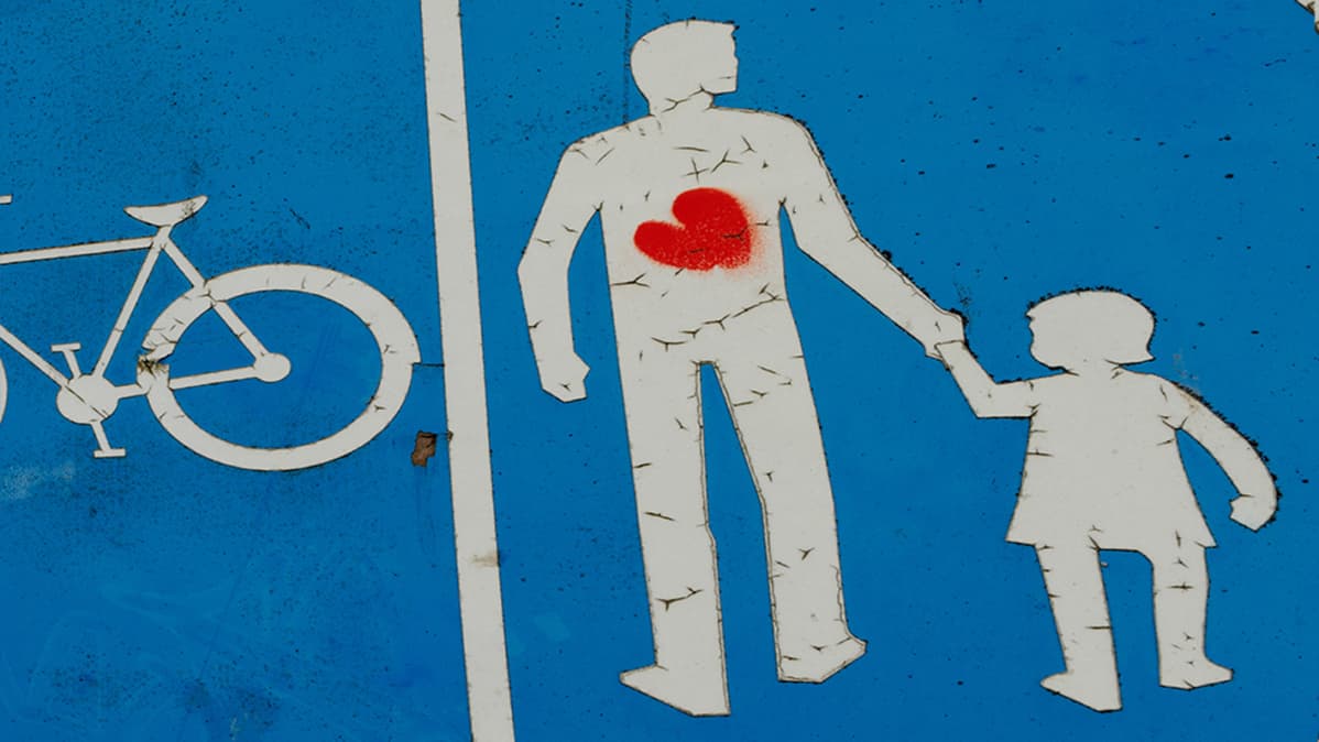 Isä taluttaa lasta tieliikennekyltissä.