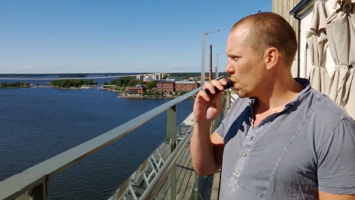 Mies polttaa terassilla sähkötupakkaa