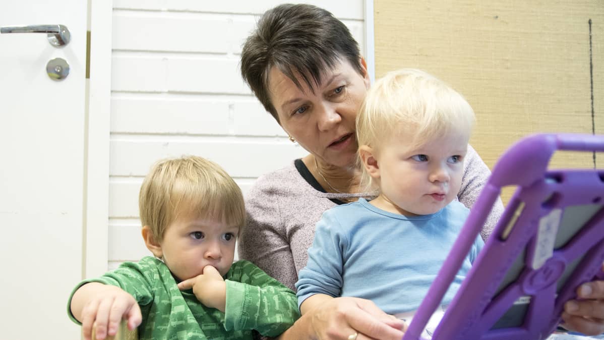 Tarja Kemppainen pelaamassa tabletilla kahden lapsen kanssa.