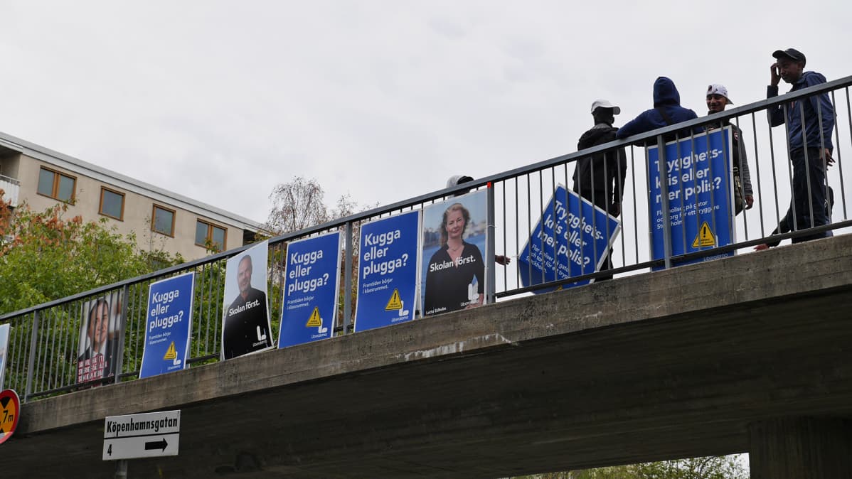 Ihmisiä kylttien kanssa sillalla.