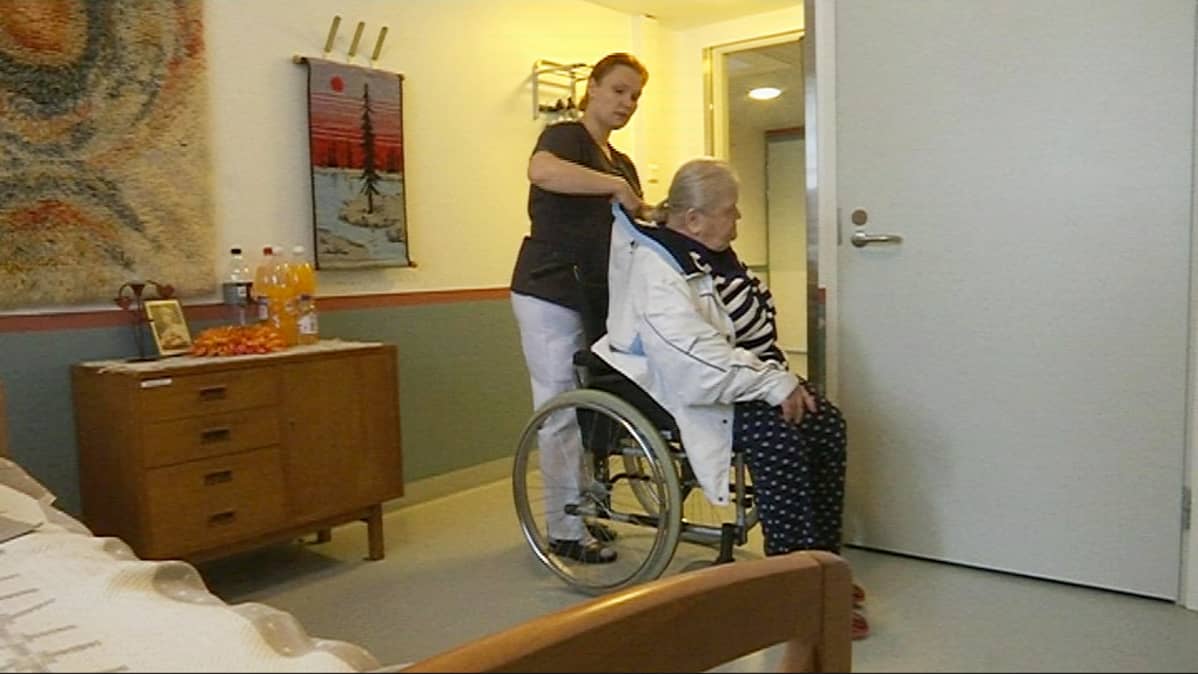 Sairaanhoitaja Niina Inkiläinen pukee Elsa Mentulalle ulkotakkia.