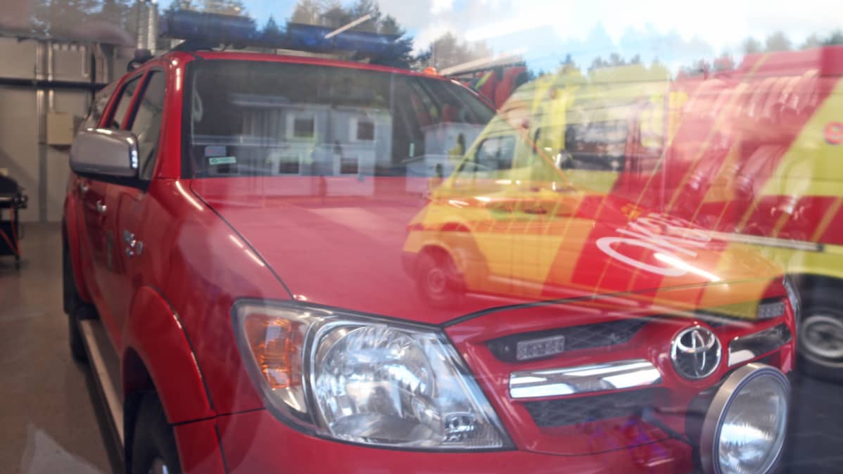 Hailuodon paloaseman johtoauto tallissa, ensivasteen sairasauto heijastuu ikkunasta.