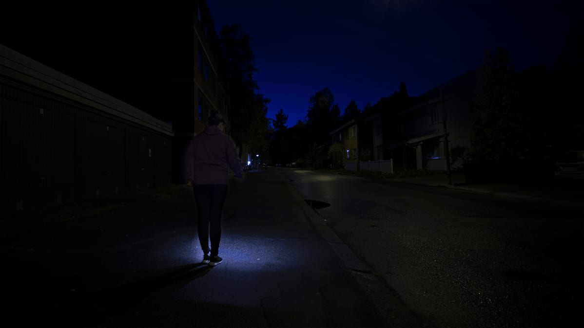Nainen kävelee pimeässä kännykän valossa