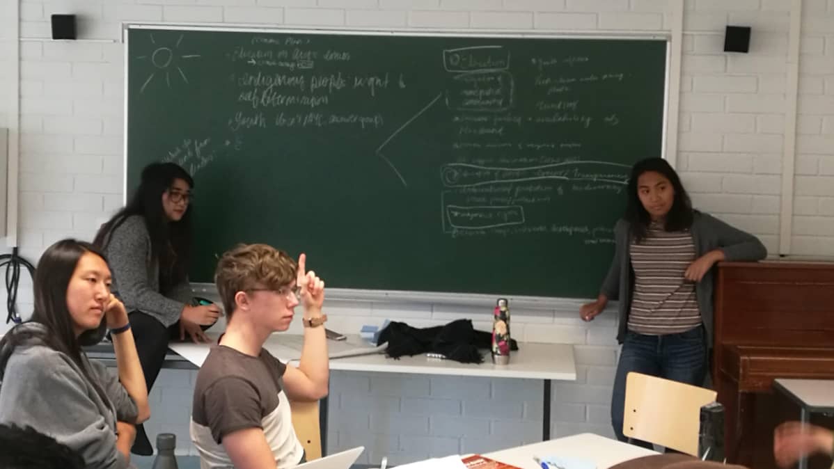 Liitutaululla vasemmalta: Alliana Marie Salanguit, Eva Wu, Jone Måsøy. Keskellä Kaustubh Srikanth. Oikealla takana Tasha Elizarde ja oikealla edessä Juhán Niila Stålka. Nuoret suunnittelevat luokassa julkilausumaansa.