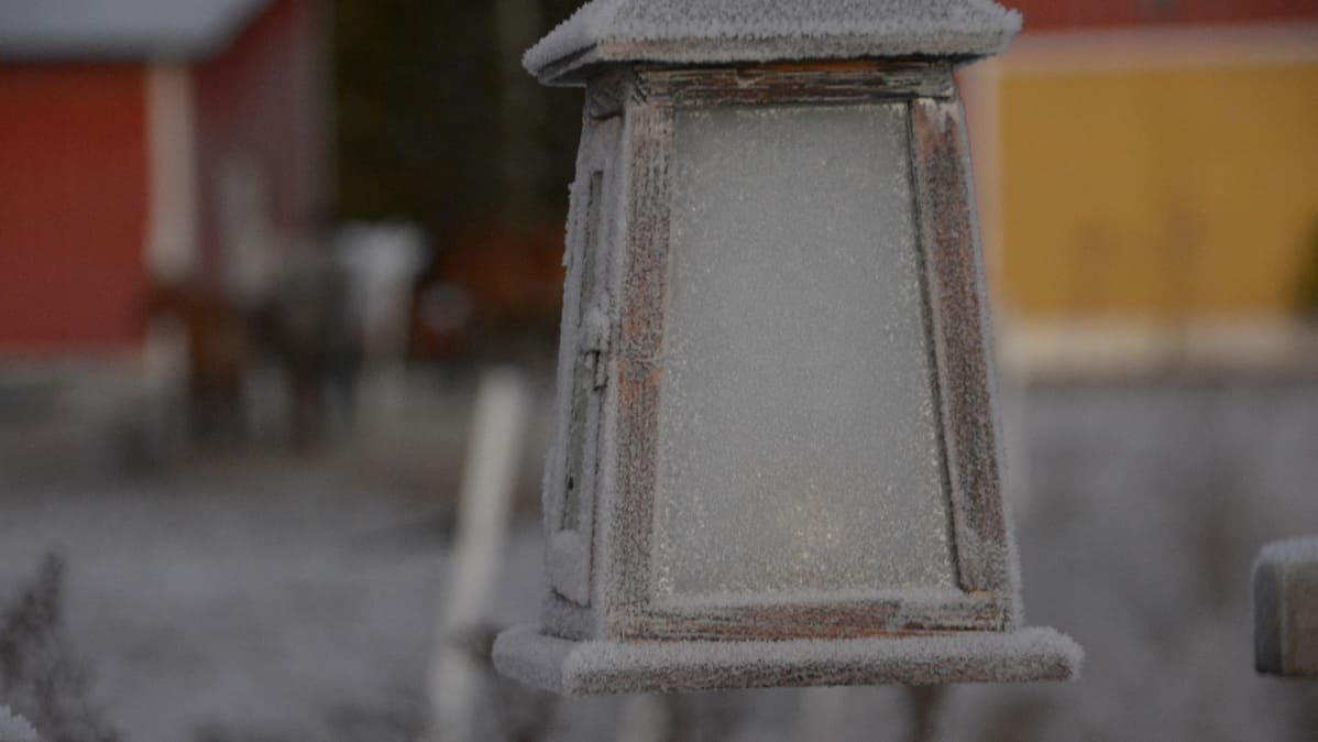 Huurteinen lyhty, taustalla keltaovinen, punainen tallirakennus.