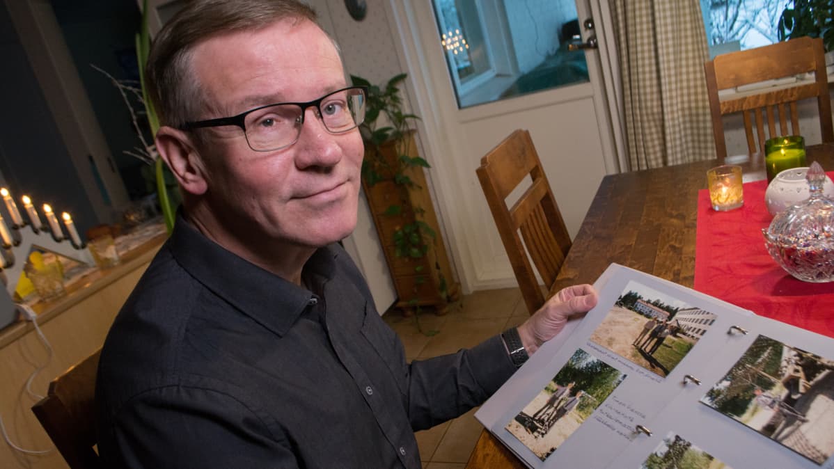 Heikki Helve selaa oman varusmiespalvelusaikansa kuvia kotipöytänsä ääressä.