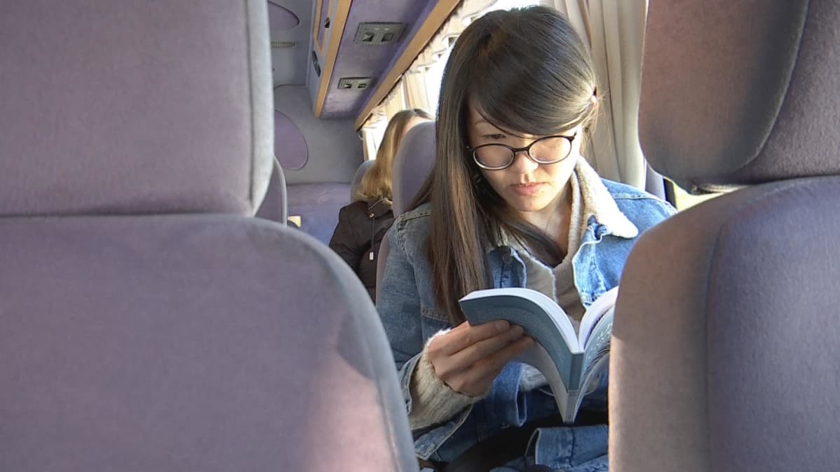 Nainen lukee bussissa kirjaa.